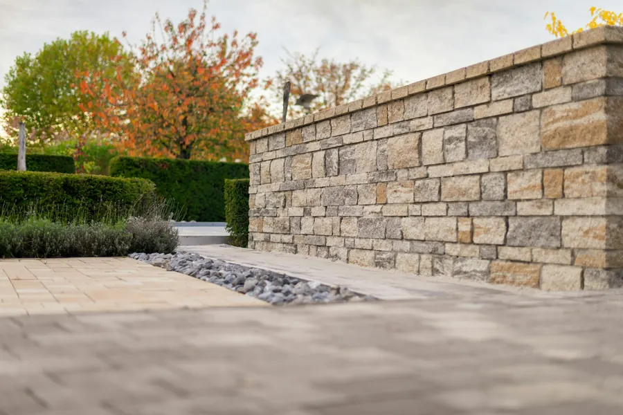Sandstone-coloured block wall with paving and autumn trees